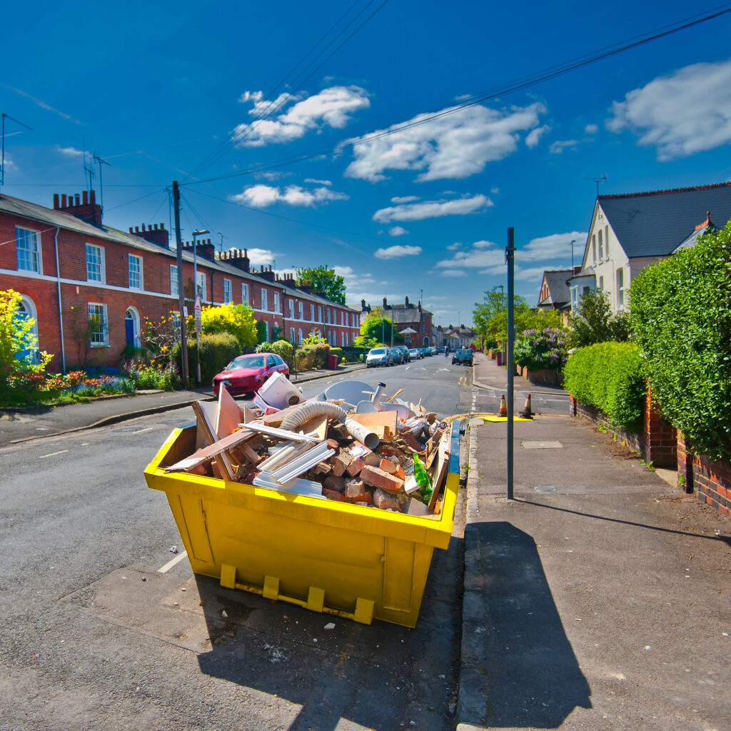 yellow dumpster in a neighborhood with junk and trash piled into it