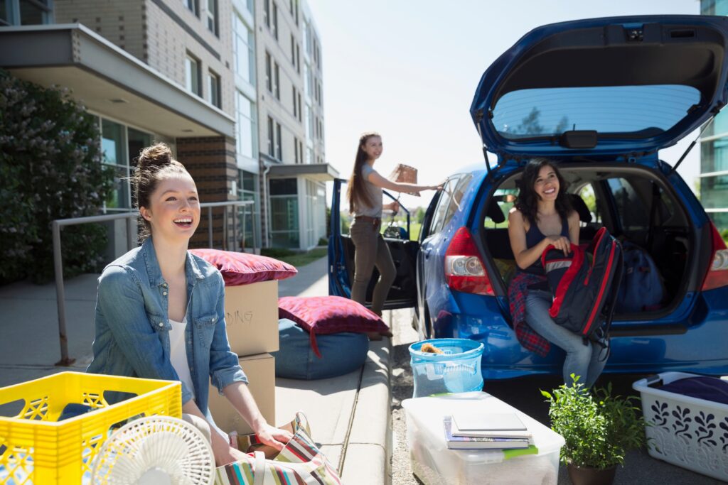 girls moving out of college dorm with boxes and bins