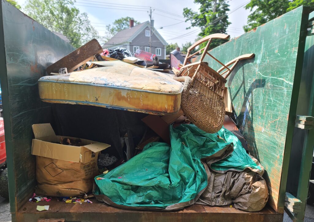 hoarder home cleanout with items stacked in a dumpster bin