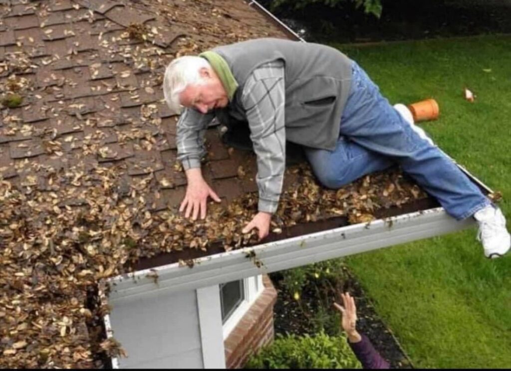 older man struggling to clean leaves out of the gutters on his roof