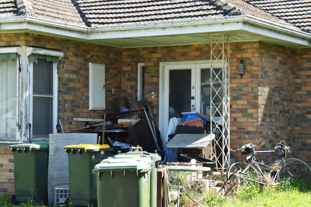 outside view of hoarder home with excess junk on the porch and driveway